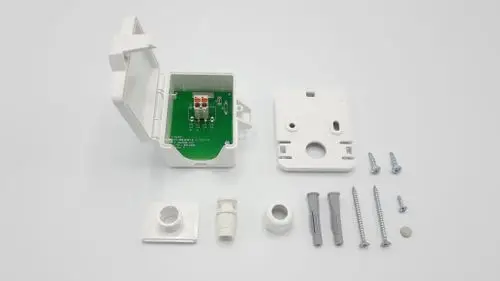 Weiße Kunststoffbox mit einer offenen Vorderseite, innen beschaltete Platine und Zubehörteilen wie Schrauben und Dübel. Teile für Außentemperaturfühler von Remeha.